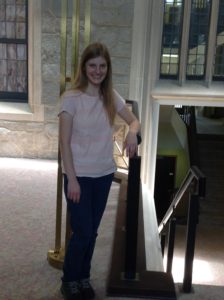 A student worker leans on the stacks, smiling