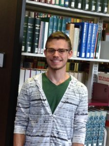 A student worker leans on the stacks, smiling