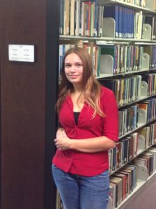 A student worker leans on the stacks, smiling