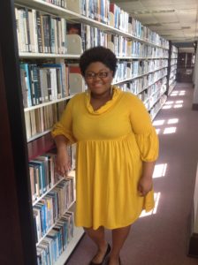 A student worker leans on the stacks, smiling