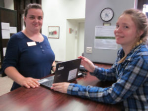 A student and worker in the library pose with a laptop